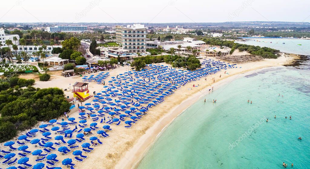 Aerial bird's eye view of famous Makronissos beach coastline, Ayia Napa, Famagusta, Cyprus. The landmark tourist attraction Makronisos bay at sunset with golden sand, sunbeds, sea restaurants in Agia Napa on summer holidays, from above.