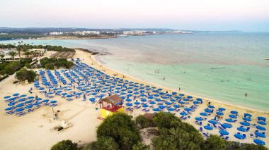 Ünlü Makronissos sahil şeridi Ayia Napa, Famagusta, Kıbrıs 'ın havadan kuş bakışı manzarası. Günbatımında Agia Napa 'da altın kum, güneşlik, deniz restoranları ve yaz tatilleri ile turistik mekan Makronisos Körfezi..