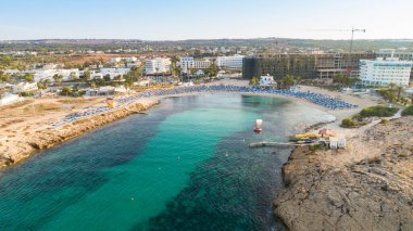Vathia Gonia plajı, Ayia Napa, Famagusta, Kıbrıs 'ın havadan kuş bakışı görüntüsü. Gündoğumunda, Agia Napa 'da yaz tatillerinde altın kum, güneşlik, deniz restoranları ve deniz restoranlarıyla turistik bölge kayalık körfezi..