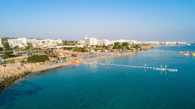 Protaras, Paralimni, Famagusta, Kıbrıs 'taki İncir ağaçlarının kuş bakışı görüntüsü. Ünlü turistik eğlence ailesi, tekneleri, güneşlikleri, restoranları, su sporları olan kumlu plajlar yaz tatillerinde denizde yüzen insanlar..
