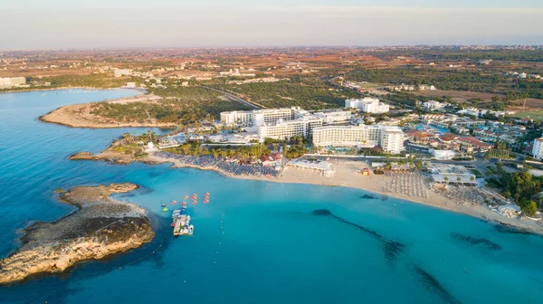 Aerial bird's eye view of famous Nissi beach coastline, Ayia Napa, Famagusta, Cyprus. The landmark tourist attraction islet bay at sunrise with golden sand, sunbeds, sea restaurants in Agia Napa on summer holidays, from above.
