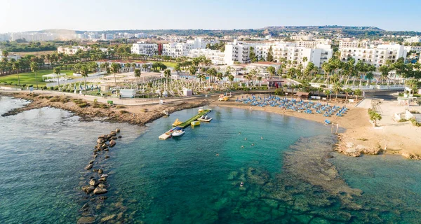 Aerial bird\'s eye view of Pernera beach in Protaras, Paralimni, Famagusta, Cyprus. The famous tourist attraction golden sandy bay with sunbeds, water sports, hotels, restaurants, people swimming in sea on summer holidays from above.