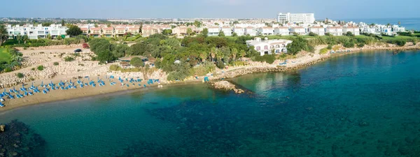 Aerial bird\'s eye view of Sirena beach in Protaras, Paralimni, Famagusta, Cyprus. The famous Sirina bay tourist attraction with sunbeds, golden sand, restaurant, people swimming in sea on summer holidays from above.