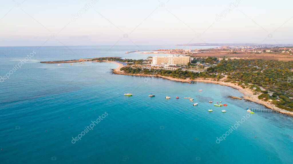 Aerial bird's eye view of Landa beach, Ayia Napa, Famagusta, Cyprus. The landmark tourist attraction golden sand bay at sunrise with sunbeds, sea restaurants between Makronissos and nissi in Agia Napa on summer holidays, from above.