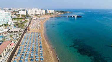 Protaras, Paralimni, Famagusta, Kıbrıs 'taki Fig Tree' deki Sunrise plajının havadan kuş bakışı görüntüsü. Altın kumu, tekneleri, güneşliği, restoranları, su sporları, yaz tatillerinde denizde yüzen insanları olan ünlü turistik aile körfezi.