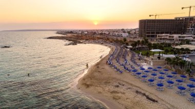 Kıyı şeridi günbatımı ve tarihi plaj manzarası yukarıdan Agia Thekla, Ayia Napa, Famagusta, Kıbrıs. Kuş bakışı gökyüzü manzarası turistlerin ilgi odağı altın kumlu körfez, adacık, Ammochostos 'taki güneşli yataklar..