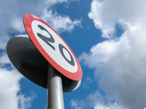 A British road speed limit sign, indicating a maximum speed of 20 miles per hour, with a blue sky and white clouds above. — Stock Image British Road Speed Limit Sign Indicating Maximum Speed Miles Hour Stock Photo