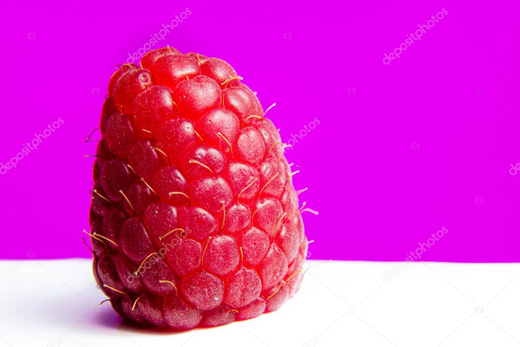 A solitary raspberry set against a bright purple background.