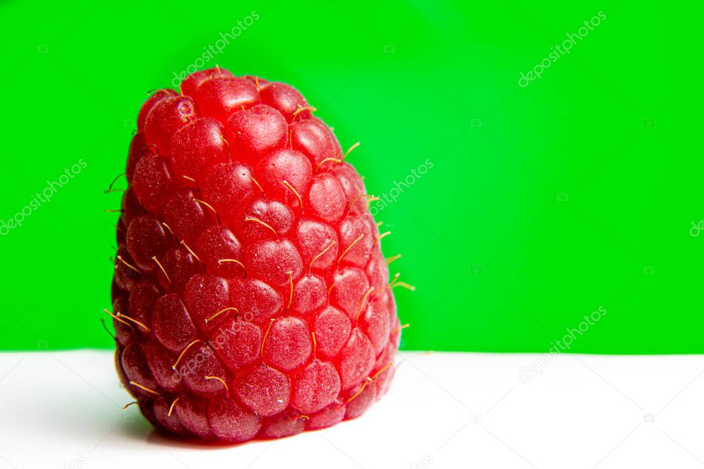 A solitary raspberry set against a bright green background.