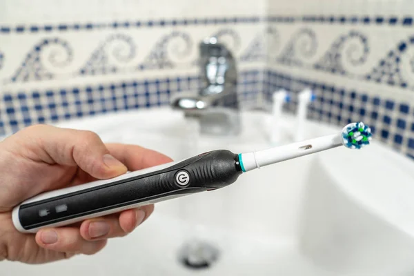 Electric Rechargeable Toothbrush with a Black Handle and five Toothbrush Heads.Light blue background.