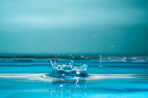 Gota de água caindo em um copo, atingindo a superfície da água.Foco selecionado — Fotografia de Stock
