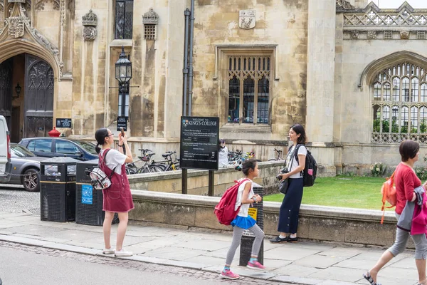 Cambridge, İngiltere, 1 Ağustos 2019. Kings Koleji önünde güneşli bir günde Cambridge caddesinde yürüyen ve fotoğraf çeken turistler