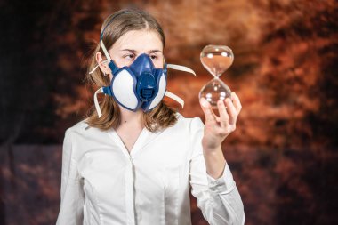 Gaz maskeli bir kadın büyük cam bir kum saati tutuyor. Coronovirus Karantina, Evde Kal Konsepti. Covid-19 salgını