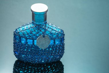 Siyah ayna arka planında yansıması olan mavi parfüm şişesi.