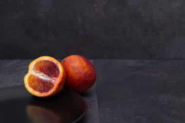 Siyah bir zemine karşı siyah bir tabakta sulu, olgun kırmızı kanlı bir portakal dilimi..