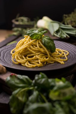 İtalyan spagettisi iştah açıcı klasik makarna, fesleğenli ve ahşap tepside. Arka planda yeşiller, salatalıklar, bir bıçak ve ahşap kaplar var..