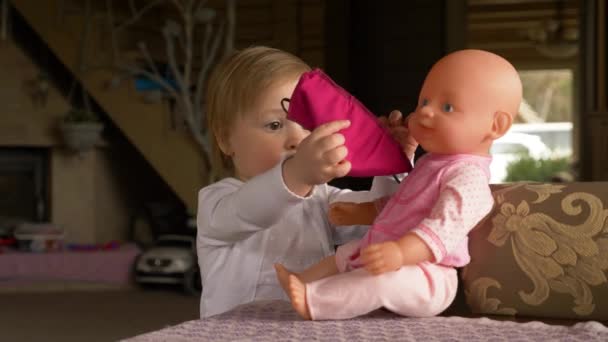 Menina bonita durante a quarentena tenta colocar uma máscara facial em sua boneca — Vídeo de Stock