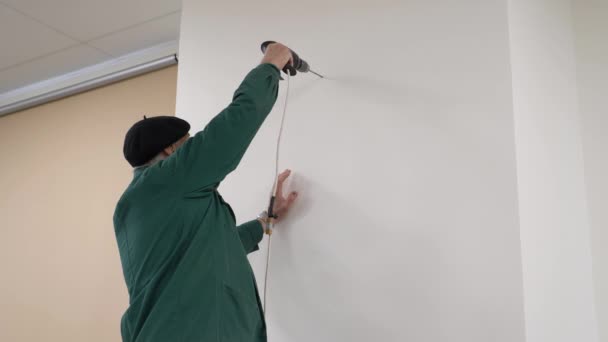 Starý řemeslník používá vrtačku, aby dal obraz na zeď. — Stock video