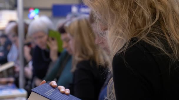 Блондинка в очках яростно ищет интересную книгу на книжной ярмарке — стоковое видео