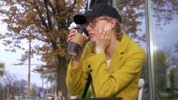 Jeune femme détendue avec casquette s'assoit et boit du café admirant la vue sur la ville — Video