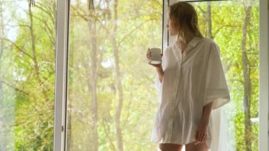Nazik hatlı kadın sabah rutinini yapıyor. Genç bir bayan ormanı sever ve sabah duşundan sonra kahve içer. Islak saçlı, makyajsız..