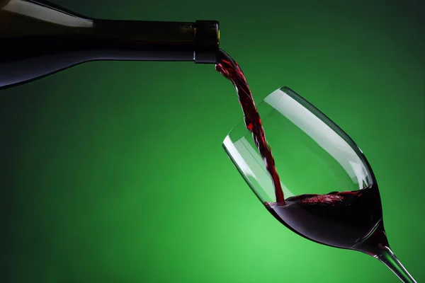 Verter vino tinto en una copa de vino sobre un fondo verde — Foto de Stock