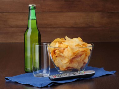 Şişe bira, boş bardak ve kase cips ile