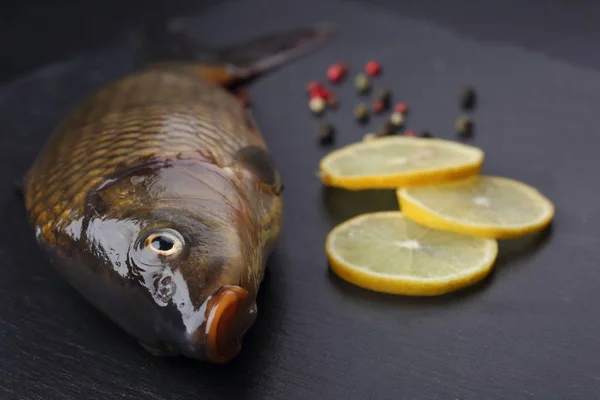 Fresh carp with peppers and lemon on black cutting board — Stock Photo, Image