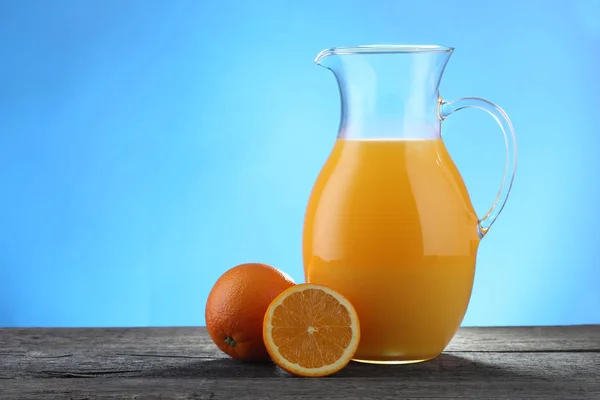 Krug Orangensaft und Orangen auf blau — Stockfoto