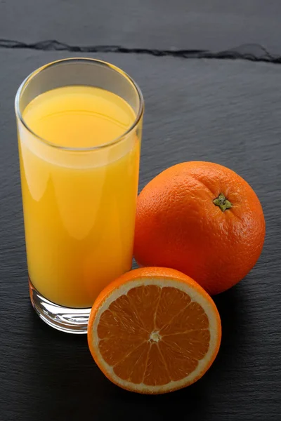 Copo de suco de laranja e laranjas na tábua de ardósia — Fotografia de Stock