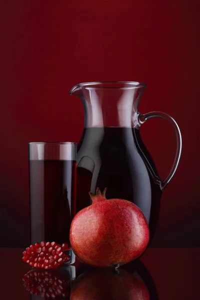 Glass and jar of pomegranate juice with fruit on red — Stock Photo, Image