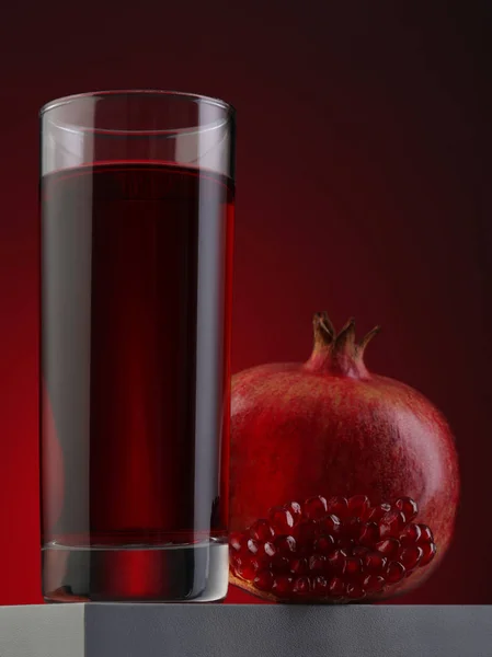 Glass of pomegranate juice and fruit  on red — Stock Photo, Image