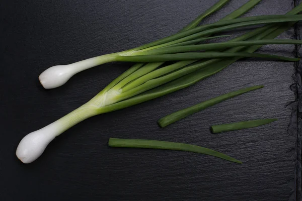 Cebolla de primavera sobre piedra de pizarra negra —  Fotos de Stock