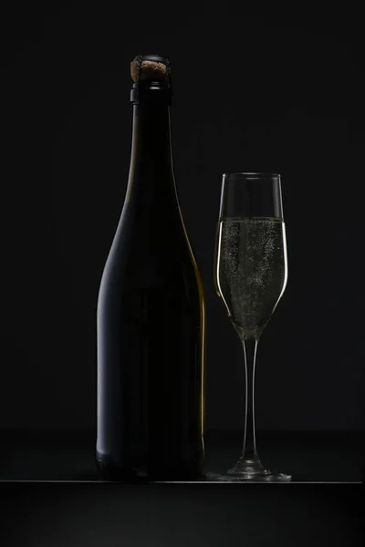 Garrafa de champanhe e vidro no fundo preto — Fotografia de Stock