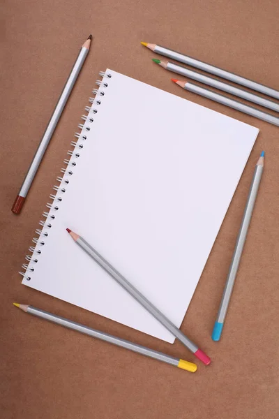 Color pencils and notebook on cardboard background — Stock Photo, Image
