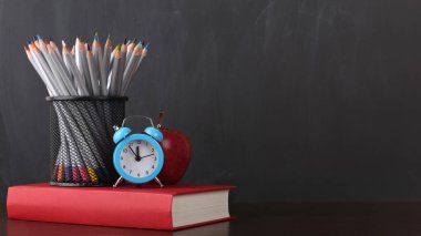 Okula geri dön. Saat, kitap, elma ve kalemler tahtada.