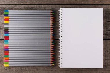 Ahşap arka planda renkli kalemler ve defter. Üst görünüm