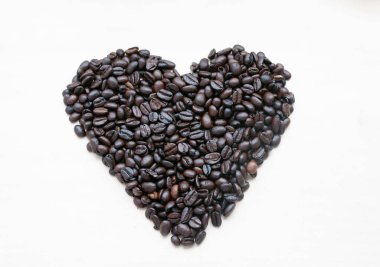 Kalbin şekli kavrulmuş kahve çekirdeklerinin hafif arka planında, mesaj için yer var..