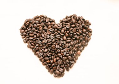 Kalbin şekli kavrulmuş kahve çekirdeklerinin hafif arka planında, mesaj için yer var..