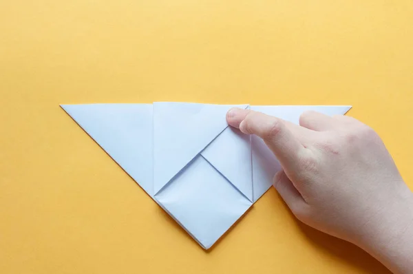Adım 8. Sarı arka plandaki bir çocuğun elleri beyaz bir kağıdın karesini üçgenlere böler. Origami boğa kavramı.
