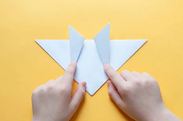 Adım 10. Sarı arka plandaki bir çocuğun elleri beyaz bir kağıdın karesini üçgenlere böler. Origami boğa kavramı.