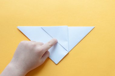 Yedinci adım. Sarı arka plandaki bir çocuğun elleri beyaz bir kağıdın karesini üçgenlere böler. Origami boğa kavramı.