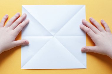 Adım 2. Sarı arka plandaki bir çocuğun elleri beyaz bir kağıdın karesini üçgenlere böler. Origami boğa kavramı.