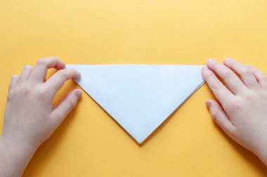 Beşinci adım. Sarı arka plandaki bir çocuğun elleri beyaz bir kağıdın karesini üçgenlere böler. Origami boğa kavramı.