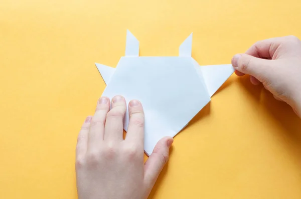 Adım 18. Sarı arka plandaki bir çocuğun elleri beyaz bir kağıdın karesini üçgenlere böler. Origami boğa kavramı.