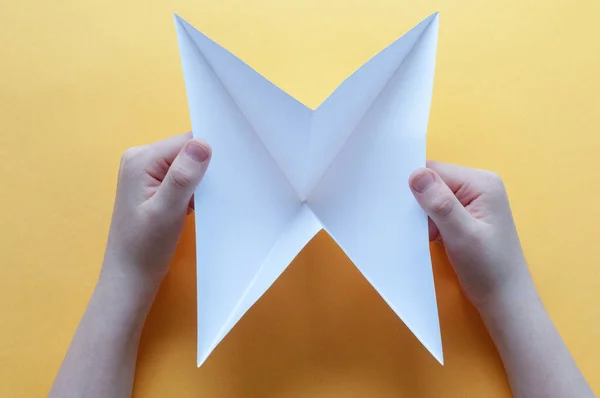 Step 3. Hands of a child on a yellow background crkflsdf.n squared white paper on triangles. Origami bull concept.