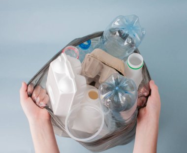 Eller, arkaplanda ayıklanmış atık, plastik, cam, şişe, kağıt ve enkaz parçaları olan bir paket tutuyor. Yakın plan. Ekoloji kavramı, atık tasnif.