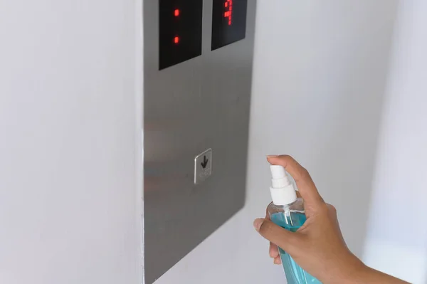 Woman hand spraying alcohol sanitizer bottle to the button control of elevator, against Novel coronavirus or Corona Virus Disease (Covid-19) at public indoor.