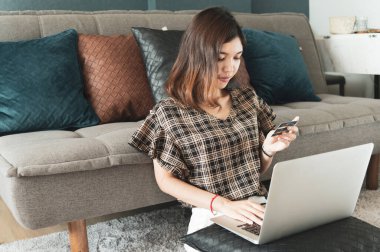 Genç Asyalı kadın kredi kartını evinde online alışveriş için kullanıyor.