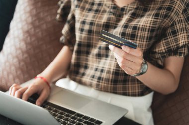 Genç Asyalı kadın kredi kartını evinde online alışveriş için kullanıyor.